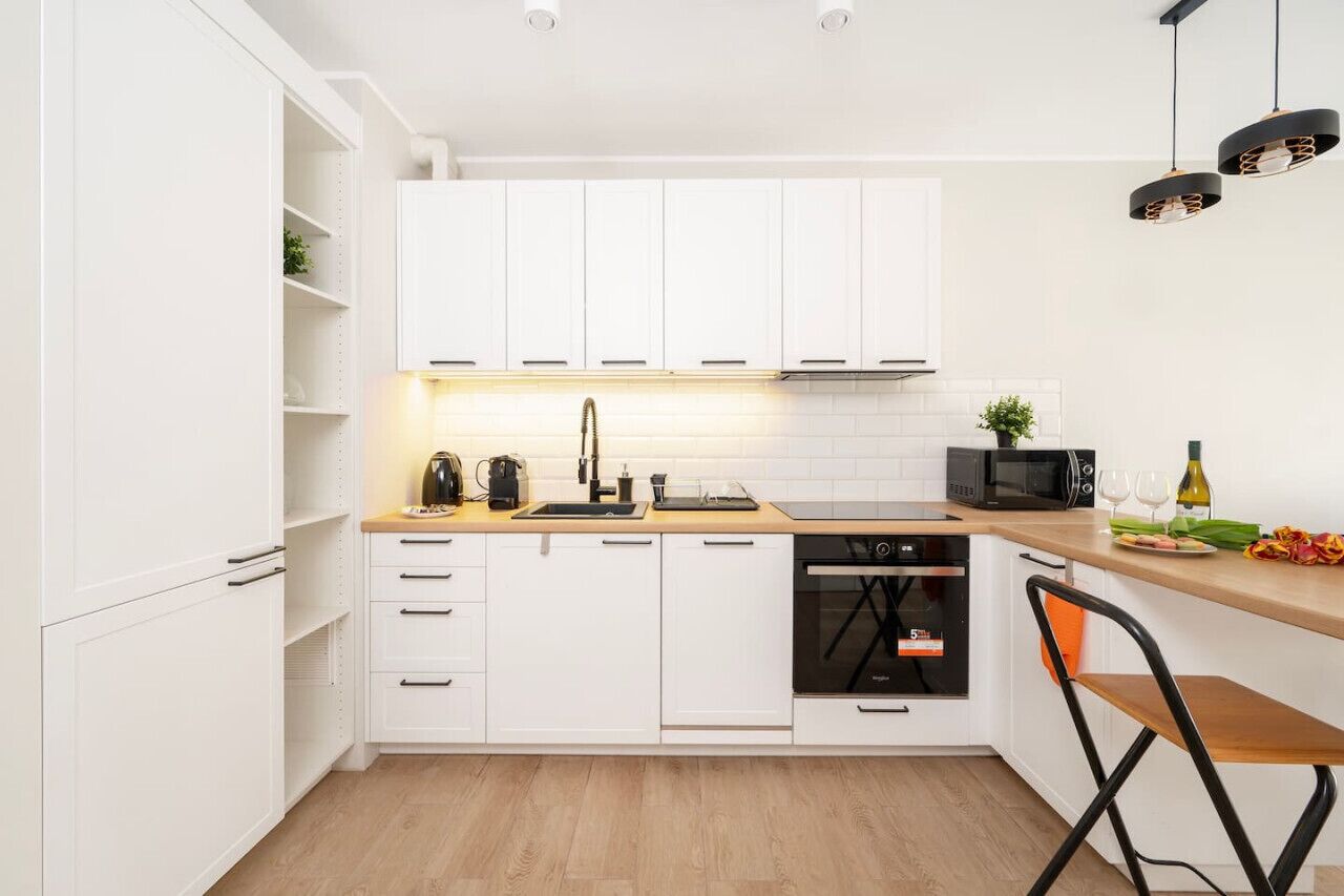 Eine moderne Küche mit weißen Schränken, einer Holzauskładung, einem eingebauten Backofen und einer schwarzen Kaffeemaschine.