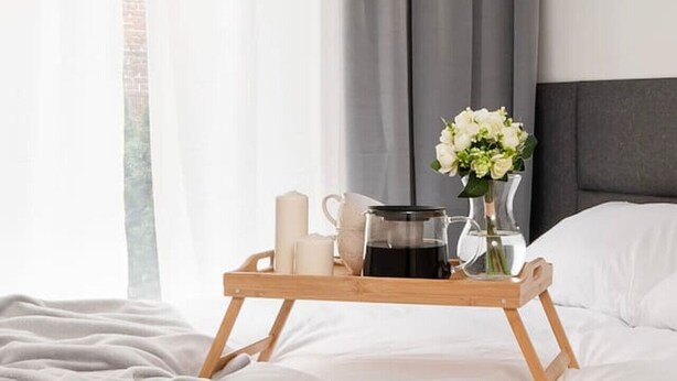 A neatly made bed with a grey blanket, a bedside table with a tray holding a coffee pot, a cup, and a vase with flowers. - Hideaway Apartment - Terrace with Garden & Parking by Rentujemy (Lódz)