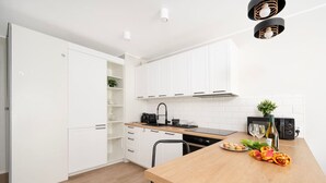 A modern kitchen with white cabinets, a wooden countertop, and a dining area. - Hideaway Apartment - Terrace with Garden & Parking by Rentujemy (Lódz)