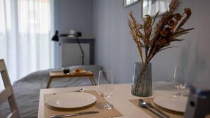 A neatly set dining table with two plates, cutlery, and a vase with dried flowers. - Warsaw Airport Studio with Private Terrace by Rentujemy (Warszawa)