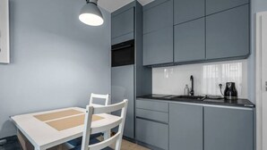 A compact kitchen with grey cabinets, a white table, and a blue chair. - Warsaw Airport Studio with Private Terrace by Rentujemy (Warszawa)
