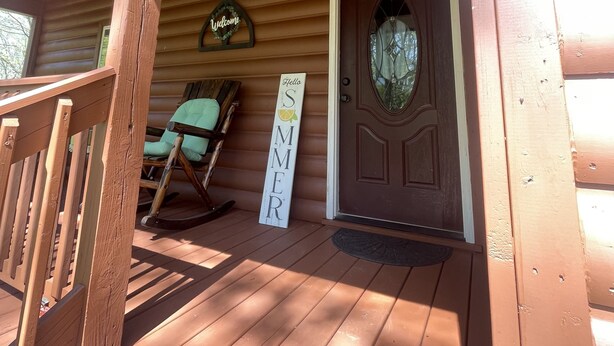 A wooden porch with a rocking chair and a sign that reads "Hello Summer." - Peaceful Cabin Steps Away From The Creek, Convenient Access To ATV Trails! (Mena)