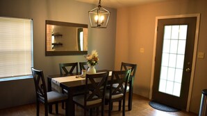A dining area with a table, chairs, a vase with flowers, a mirror, and a door. - Peaceful Cabin Steps Away From The Creek, Convenient Access To ATV Trails! (Mena)