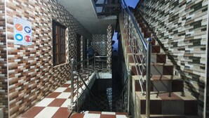 Un pasillo con piso a cuadros, una escalera con barandales de metal y paredes de ladrillo con diseño.