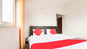 Una cama bien hecha con una colcha blanca y roja, dos almohadas rojas y un cabecero de madera.