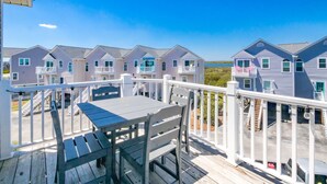 A wooden deck with a table and chairs, overlooking a row of houses with balconies, under a clear blue sky.