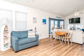 A living room with a blue sofa, a dining table with chairs, and a TV mounted on the wall.