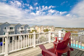 A wooden deck with red Adirondack chairs overlooking a row of beach houses with balconies.