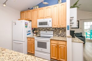 A modern kitchen with wooden cabinets, a white refrigerator, a microwave, and a stove. - Followin' The Son Too - 3 BR in Calinda Cay; Comm. Pool & Ocean Views (North Topsail Beach)