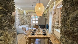 A dining area with a wooden table set for six, surrounded by stone walls and a hanging woven light fixture. - The Stone House (Kakodiki)