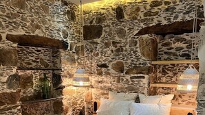 A bedroom with a stone wall, a wooden bed frame, and two bedside tables with lamps. - The Stone House (Kakodiki)