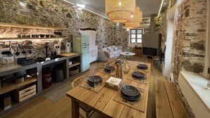 A modern kitchen with stone walls, a dining area with wooden tables, and a fireplace. - The Stone House (Kakodiki)