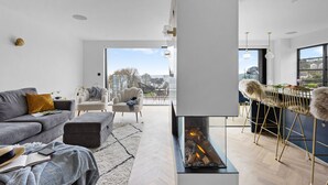 En moderne stue med pejs, grå sofa og udsigt til naturen.