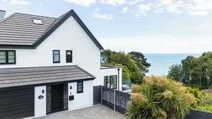 Et moderne hus med to etager, stor garage, sort hegn og havudsigt.