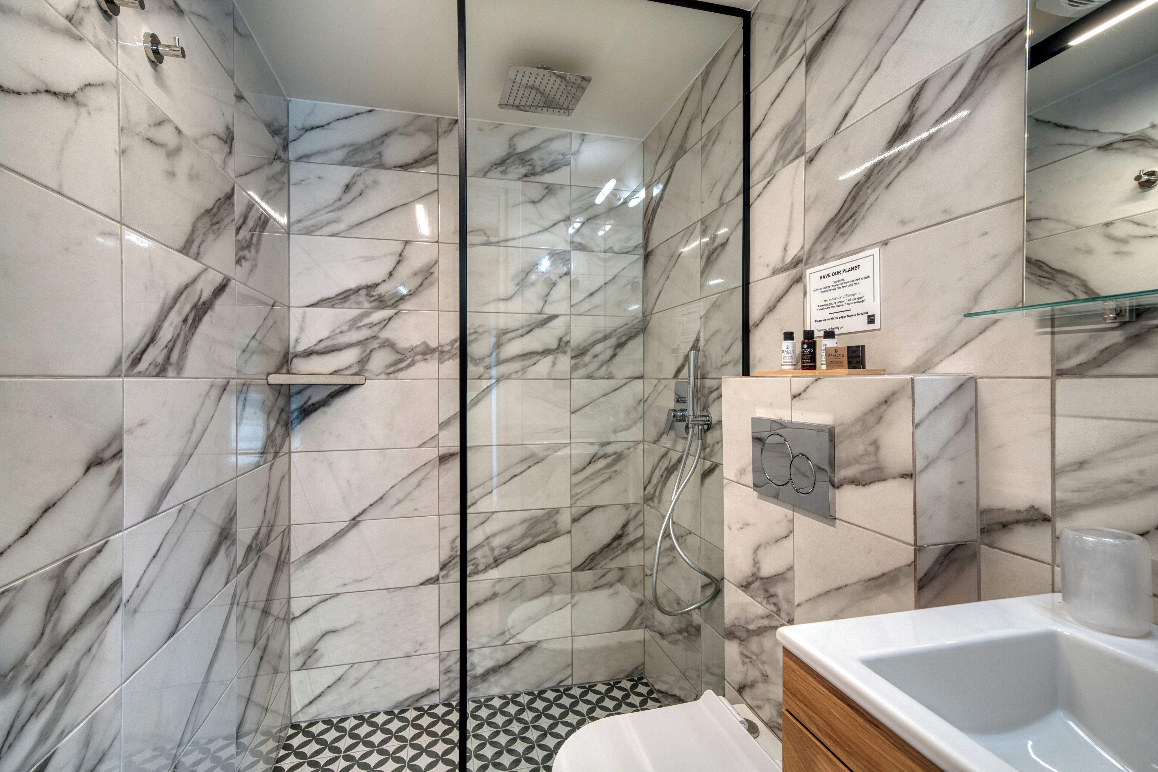 Et moderne badeværelse med marmorfliser, et glasbadeværelse, en vask og et toiletbord.