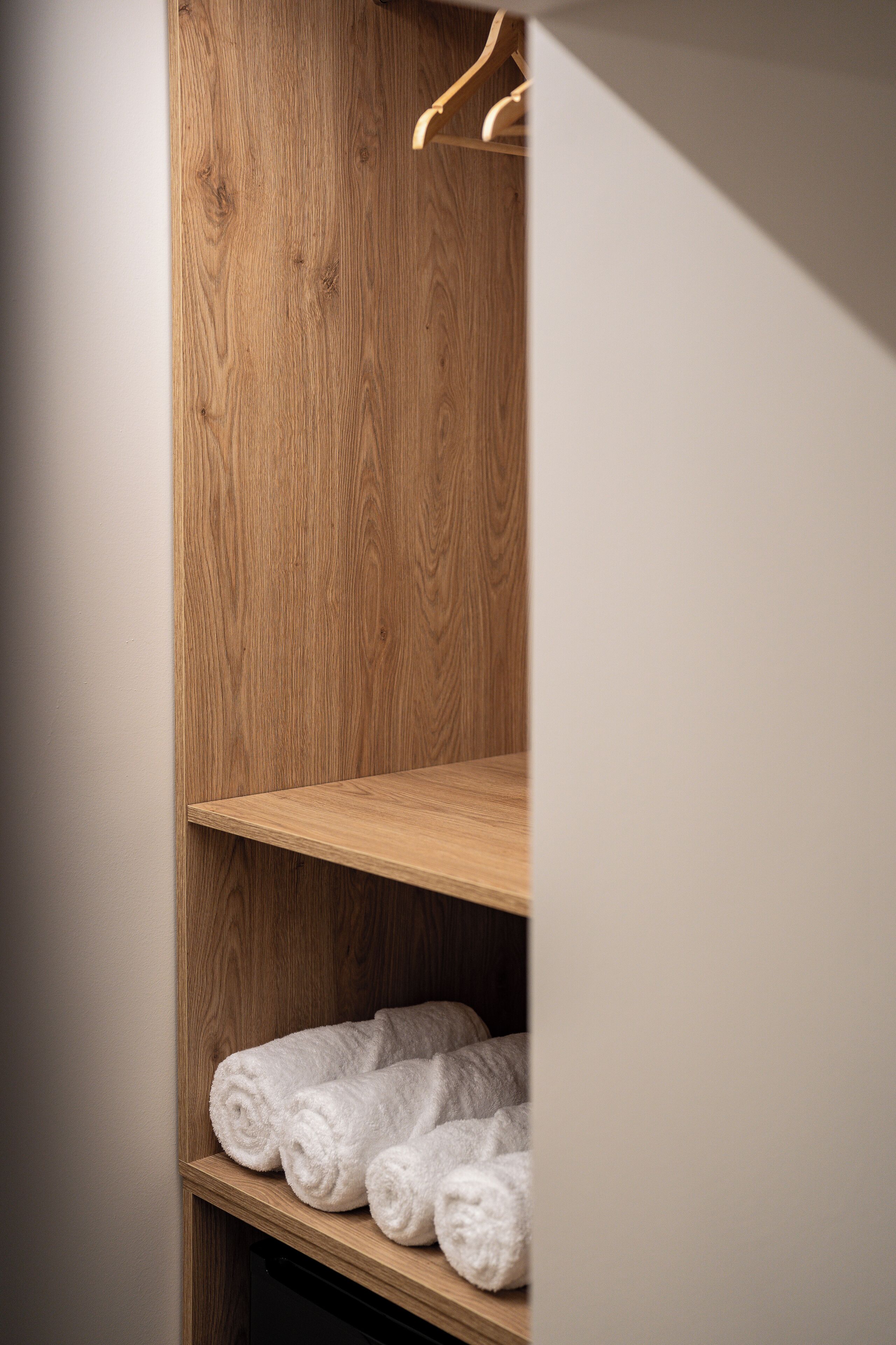 A wooden closet with shelves holding rolled white towels.