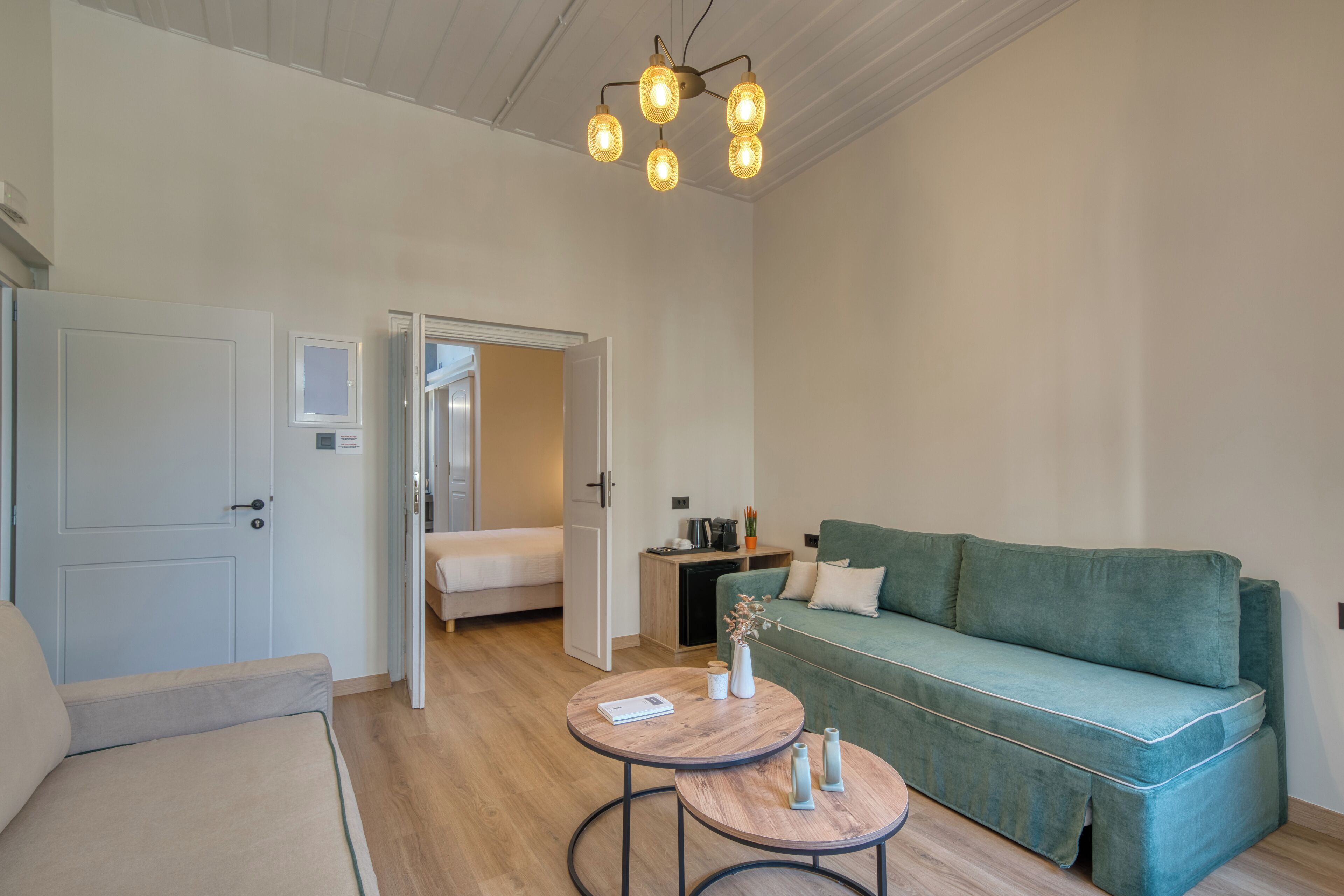 Una habitación amplia con un sofá verde, dos mesas redondas, una cama y una lámpara en el techo.