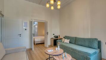 Una habitación amplia con un sofá verde, dos mesas redondas, una cama y una lámpara en el techo.