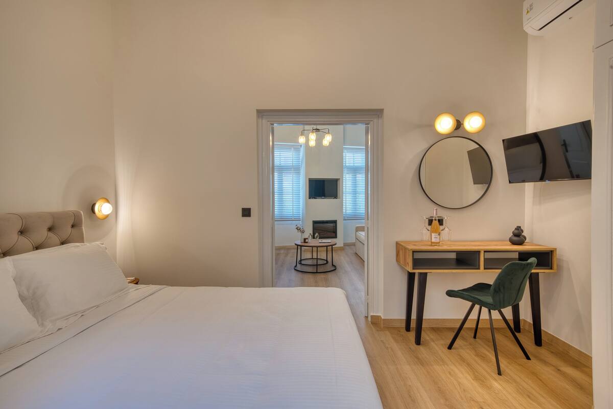 Un dormitorio moderno con una cama grande, un escritorio con silla, un televisor y un espejo.