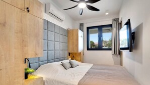 A modern bedroom with a bed, wooden wardrobe, grey padded headboard, bedside table with lamp, and a window with curtains. - Villa Valena Apartment 1 with Cooling Pool (Kralendijk)