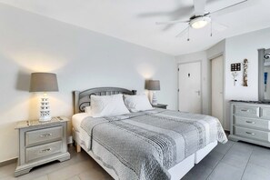 Une chambre à coucher comprenant un lit, des tables de chevet, un ventilateur de plafond et une commode.