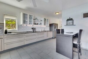 Une cuisine moderne avec des meubles blancs, un îlot central intégré et un coin repas agrémenté de meubles en osier.