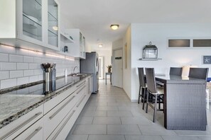 Une cuisine moderne avec des meubles blancs, un plan de travail en marbre et un coin repas doté de meubles en osier.