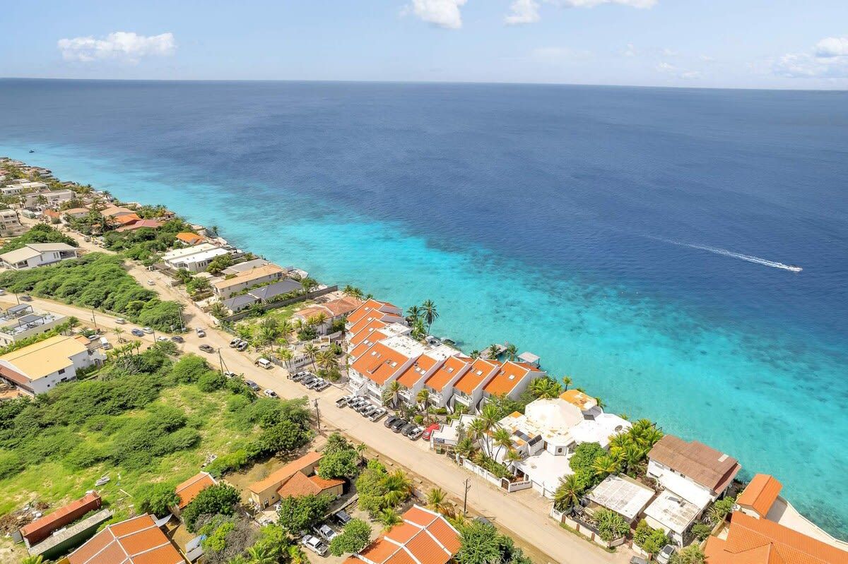 A coastal residential area with houses, a clear blue sea, and a visible boat track.