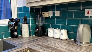 A kitchen with a washing machine, a coffee maker, and labeled containers for coffee, tea, and sugar. - Luxurious 2-bed House in Dartford (Dartford)