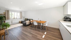 A modern living room with a dining area, a grey sofa, a wooden dining table, and a kitchen area with white cabinets. - 2 Bed 2 Bath Apt Close to Reigate Station - 2230 (Reigate)