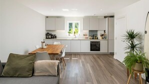 A modern kitchen with white cabinets, a wooden dining table, and a large window. - 2 Bed 2 Bath Apt Close to Reigate Station - 2230 (Reigate)