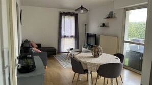 Un salon moderne comprenant un canapé, une table à manger avec des chaises, un téléviseur et une grande fenêtre donnant sur un paysage verdoyant.