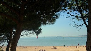 Une plage où des gens se prélassent au soleil et où un voilier flotte sur l’eau.