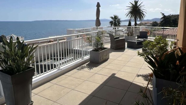 Een balkon met uitzicht op zee, plantenpotten en buitenmeubilair.