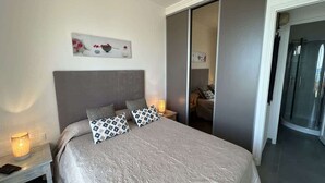 Een moderne slaapkamer met een groot bed, twee nachtkastjes met lampen, een schuifdeurkast en een douchegedeelte.