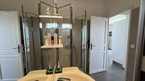 Een moderne badkamer met een douchecabine van glas, een witte wastafel met twee kraan en een plank met toiletartikelen.