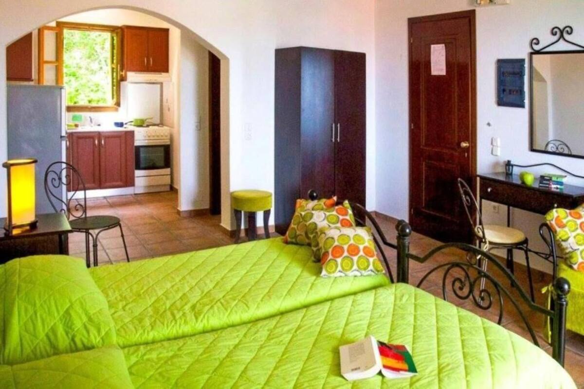 A room with a bed, a desk, a chair, a wardrobe, and a small kitchen area.