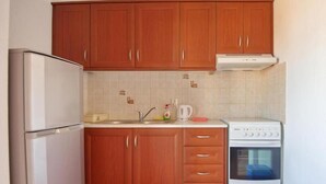 Une cuisine de taille réduite, avec des meubles en bois, un réfrigérateur blanc, une cuisinière et une poubelle bleue.