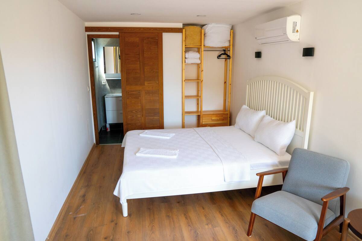 Ein Schlafzimmer mit einem Bett, einem Sessel, einem Kleiderschrank und einem Regal mit Handtüchern.
