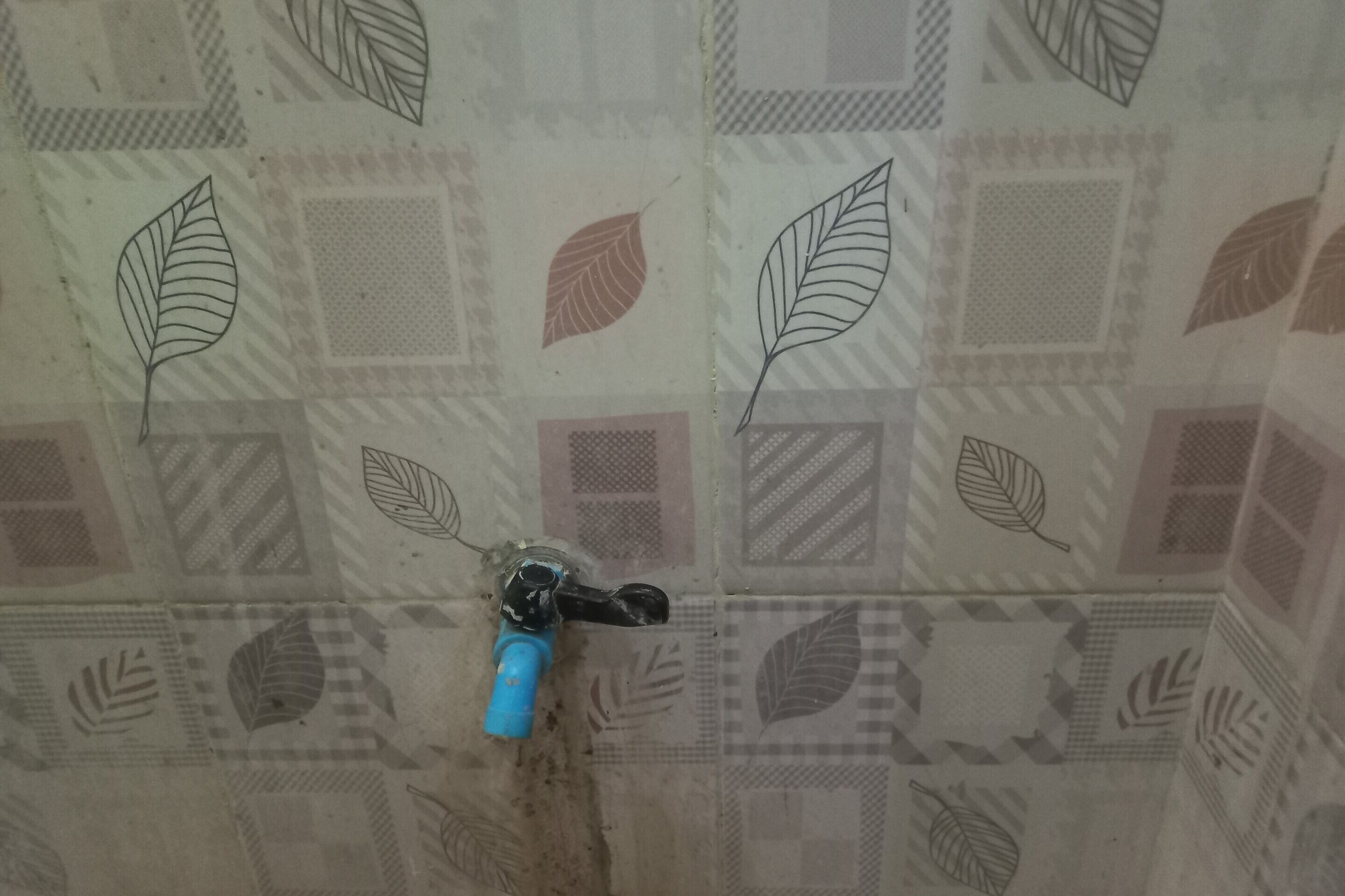 A bathroom with a patterned tile wall and a blue faucet.