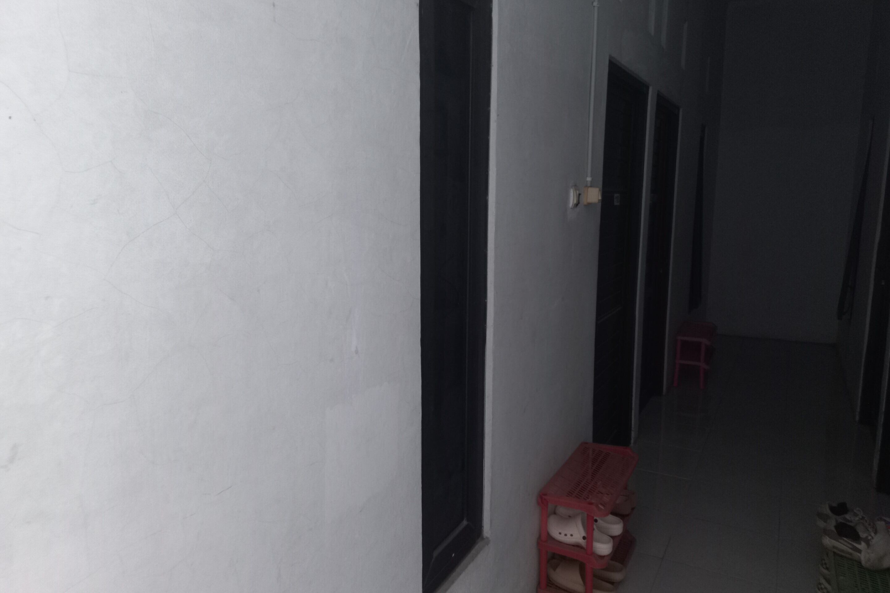 A narrow hallway with a red plastic stool and a pair of shoes on the floor.