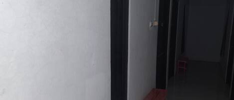 A narrow hallway with a red plastic stool and a pair of shoes on the floor.