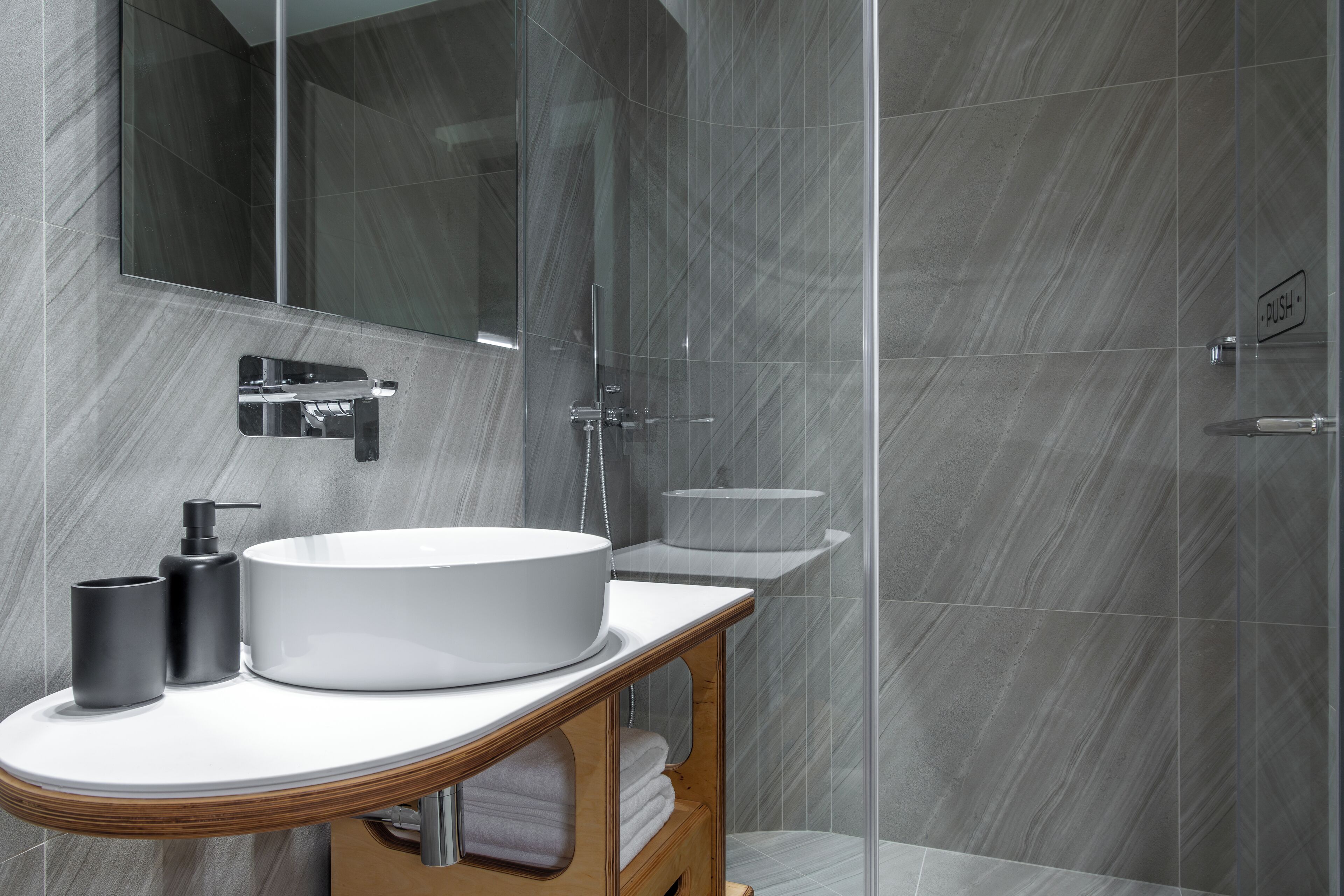 A modern bathroom with a large white sink, a mirror, and a glass shower enclosure.
