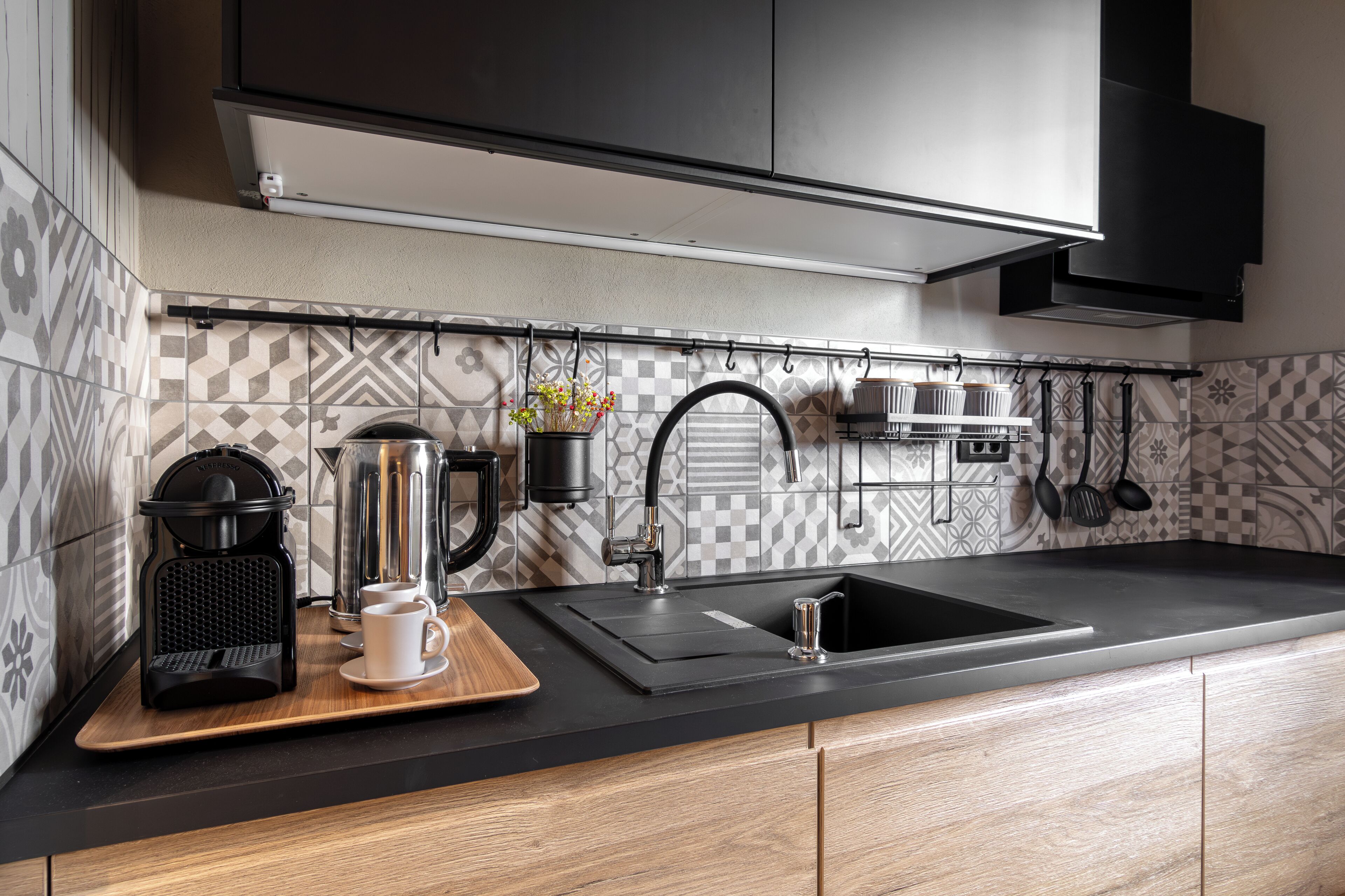 A modern kitchen with a black countertop, a coffee maker, a sink, and a backsplash with geometric patterns.
