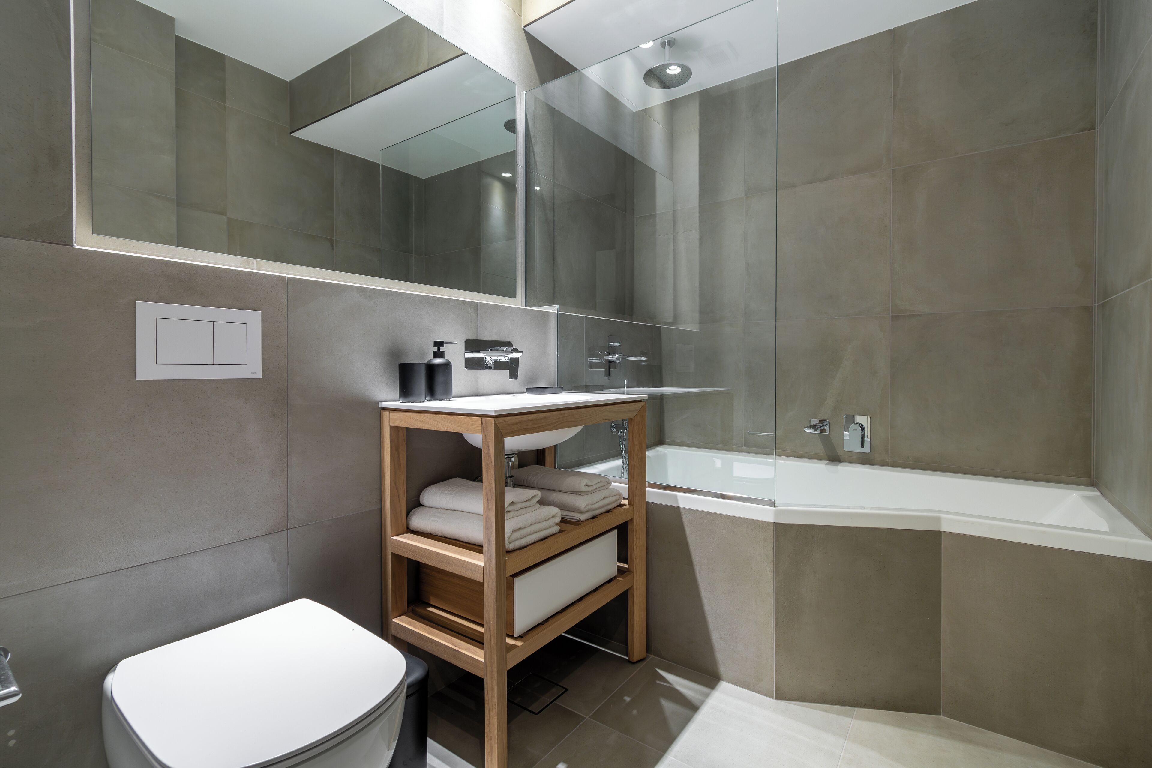 Ein modernes Badezimmer mit Toilette, einem Holzwaschtisch mit Waschbecken, einem Spiegel und einer Dusche mit Glaswand.