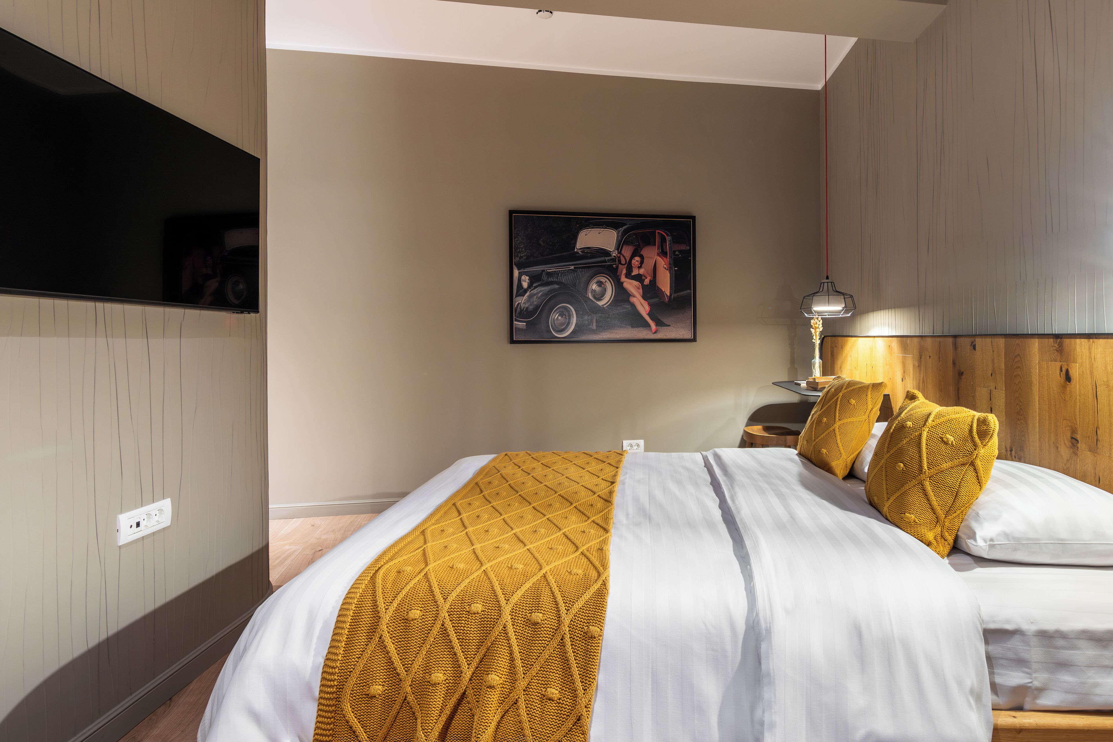 A hotel room with a bed, a nightstand, a lamp, and a wall-mounted TV.