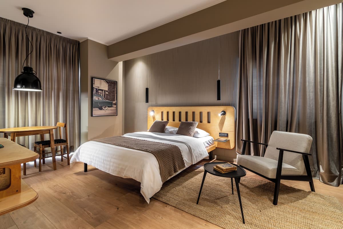 Une chambre d’hôtel moderne avec un lit en bois, un bureau, une chaise et une grande fenêtre avec des rideaux.