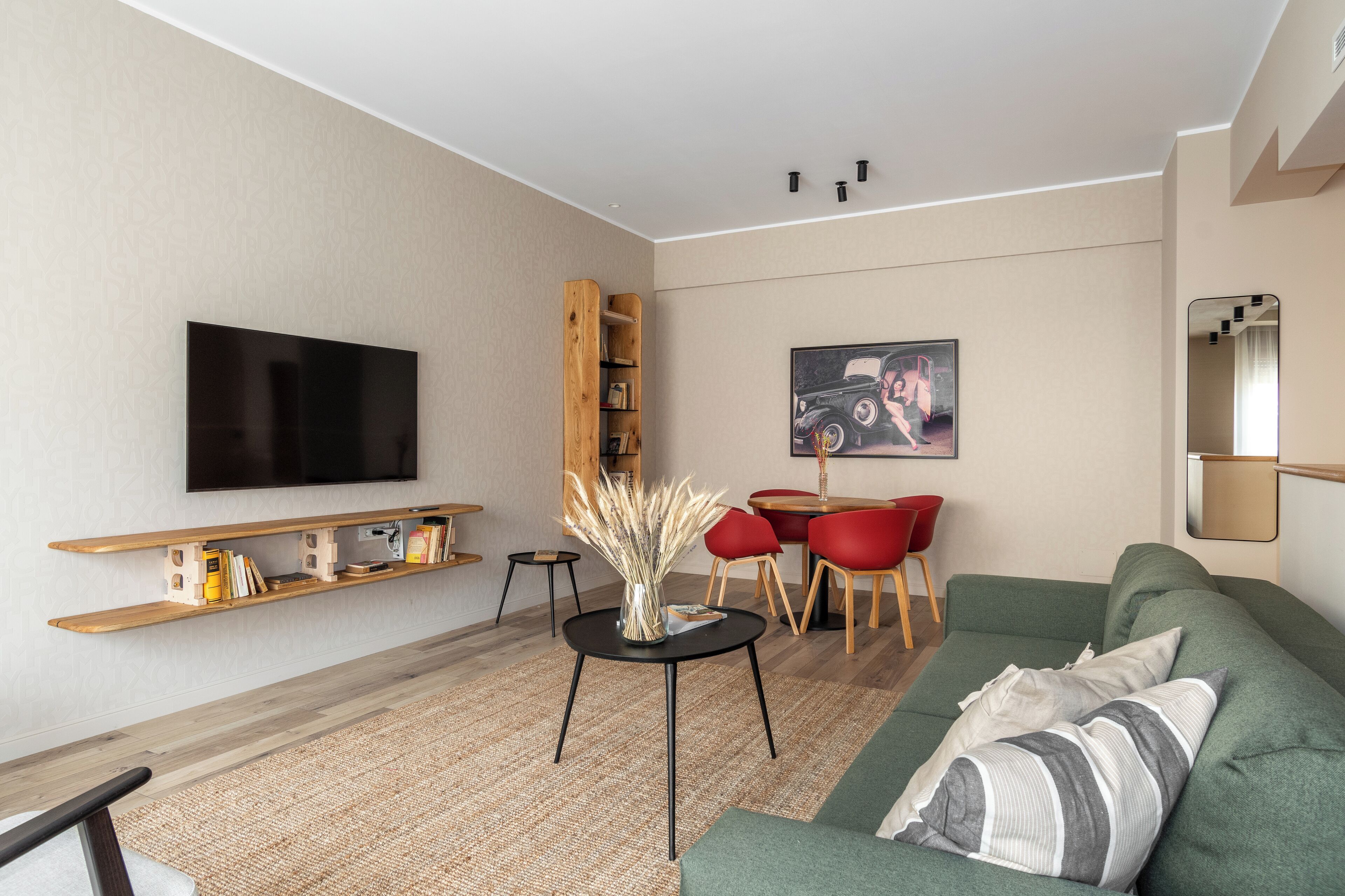 Een moderne woonkamer met een flatscreen televisie, houten planken, een ronde salontafel, een groene bank en een rode eettafelstoel.