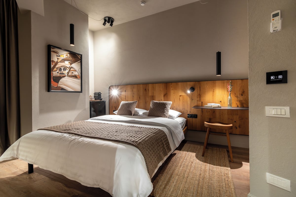 Une chambre à coucher moderne avec un grand lit, une tête de lit en bois, des tables de chevet et un petit tabouret.