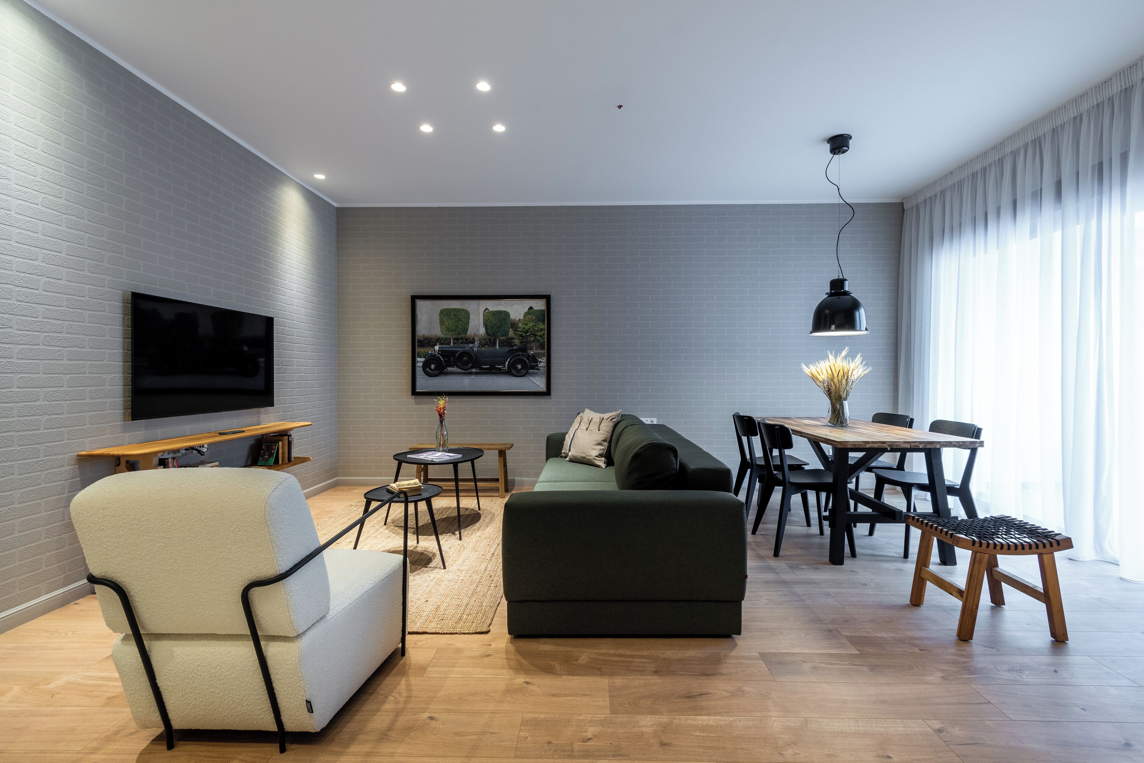 Un salon moderne avec un téléviseur à écran plat, un canapé vert, un fauteuil blanc, une table à manger avec des chaises et un banc en bois.
